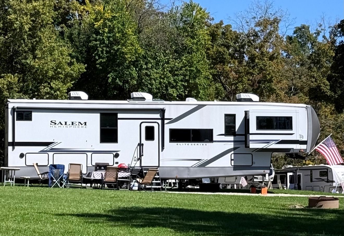 Our fifth wheel set up at a campsite with chairs out and a flag flying